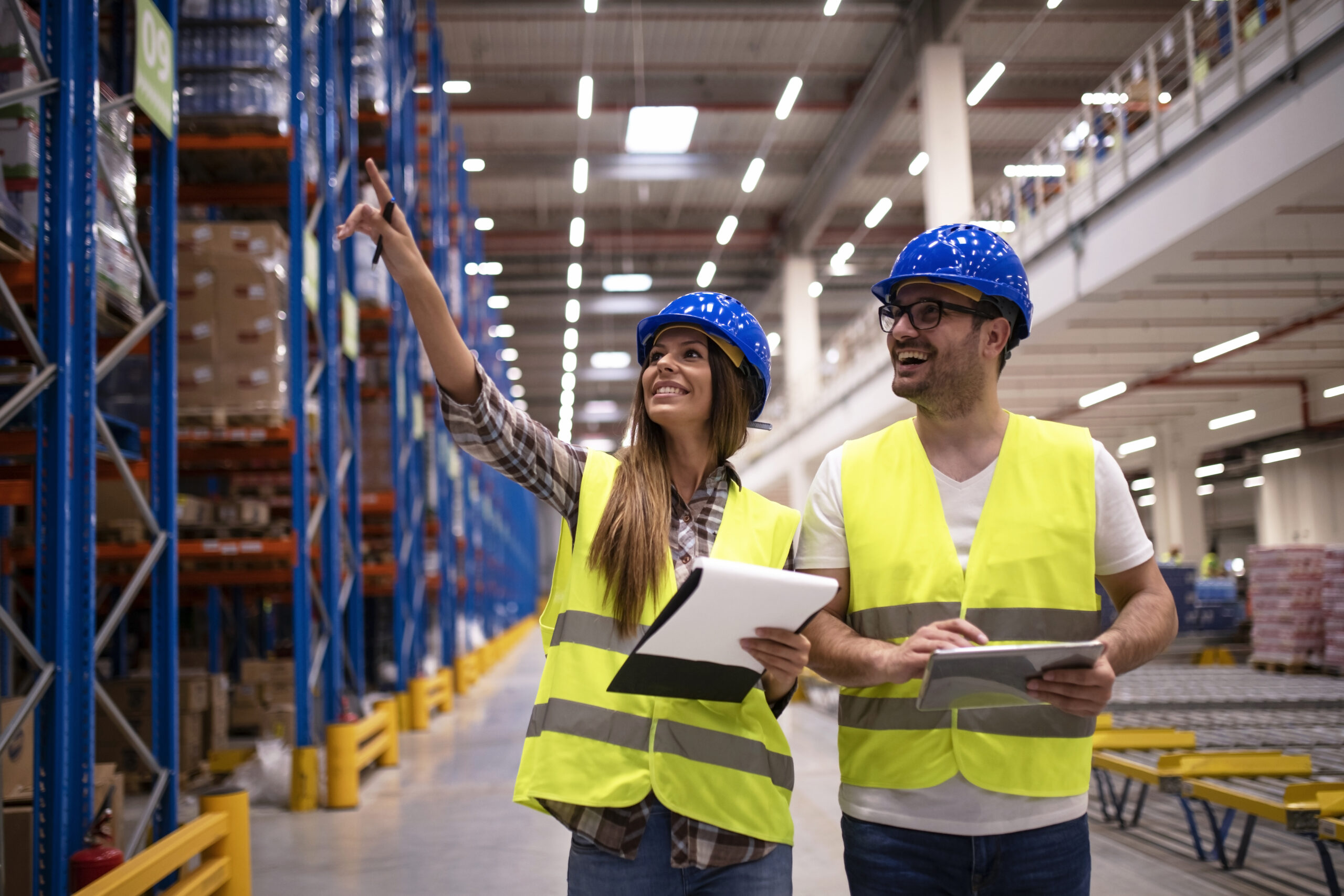 Warehouse workers in protective uniform walking through large distribution center organizing goods distribution.